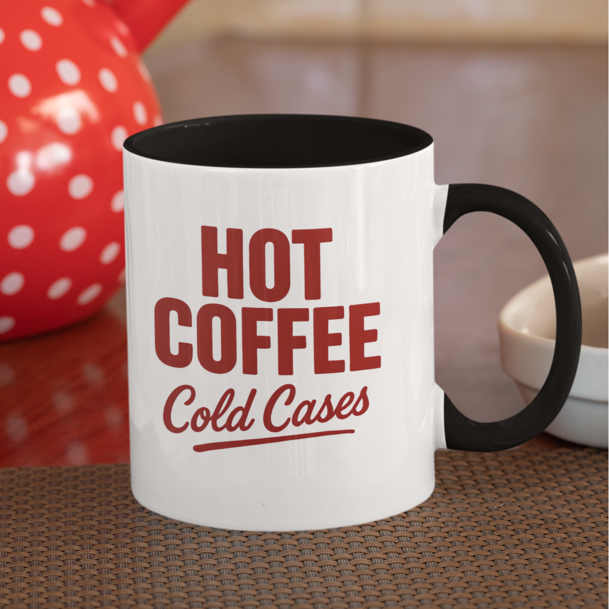 White mug with red text 'Hot Coffee Cold Cases' in a kitchen setting with a red polka dot teapot.